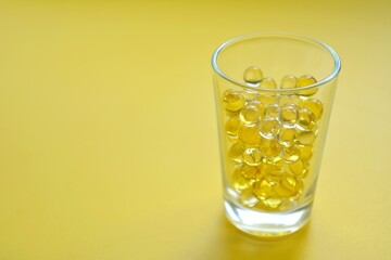 Vitamins capsules oil in glass cup yellow background