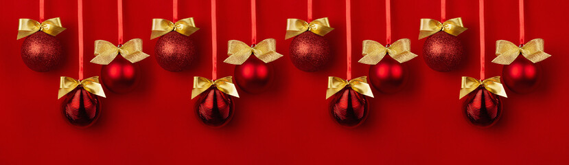 Fototapeta na wymiar Rich christmas banner in modern style for design of festive website, header. Pattern of shimmer glossy glitter balls with golden bows hang on ribbons in row on saturated red backdrop.