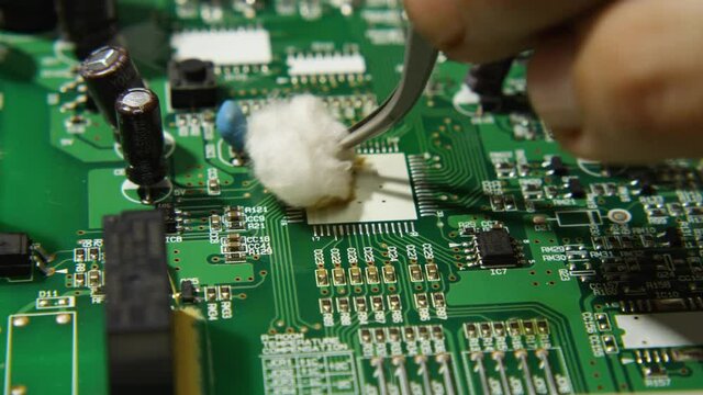 Macro video using tweezers and absorbent cotton the repairman wipes the seating on the board to install the processor. Electronics, computer, phone and TV repair shop