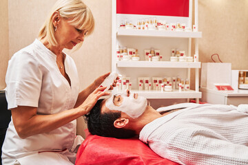 Beauty therapist applying facial cream on male customer