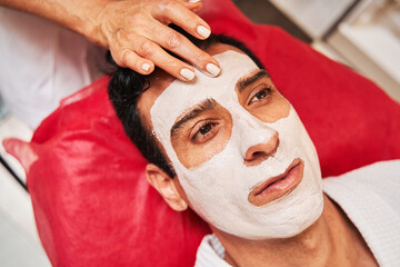 Beauty specialist applying facial pack on adult forehead