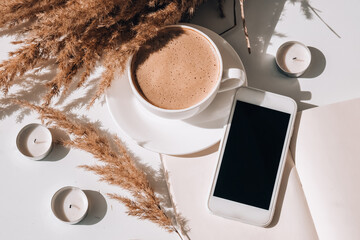 Pampas grass and white cup with coffee. Mobile phone with black screen. Checking social media Drinking Cappuccino in the breakfast morning at home. Flat lay. Wallpaper. Aesthetics