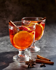 Wine glasses of hot mulled wine with spiced, apple and orange on dark background. Christmas traditional warming drink with cinnamon, cardamom and anise.