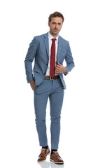 attractive young man adjusting blue suit and holding hand in pocket