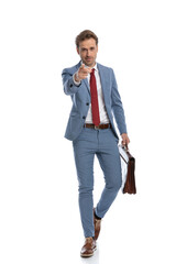 happy young businessman holding suitcase and pointing finger