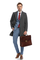 confident young man in suit with briefcase holding hand in pocket