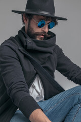 dramatic casual man squatting, looking away and wearing sunglasses