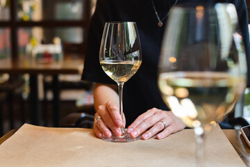 A glass of white wine in the hands of a girl relaxing in a restaurant. Tasting of alcoholic beverages. Summer rest. Romantic evening aperitif. Close-up of a glass of wine. Enjoy the moment