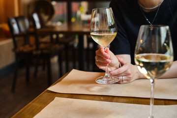 A glass of white wine in the hands of a girl relaxing in a restaurant. Tasting of alcoholic beverages. Summer rest. Romantic evening aperitif. Close-up of a glass of wine. Enjoy the moment