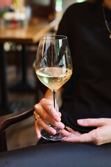 A glass of white wine in the hands of a girl relaxing in a restaurant. Tasting of alcoholic beverages. Summer rest. Romantic evening aperitif. Close-up of a glass of wine. Enjoy the moment