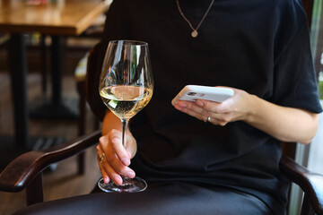 
A glass of white wine in the hands of a girl relaxing in a restaurant. Tasting of alcoholic beverages. Summer rest. Romantic evening aperitif. Close-up of a glass of wine. Enjoy the moment