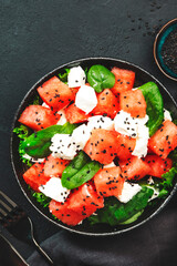 Watermelon salad bowl with feta cheese, spinach and black sesame seed, dark background, top view, copy space