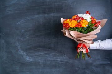 A bouquet of flowers in paper wrapping paper in a man's hand on the background of a chalk board....