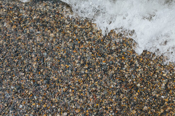 Small wet pebbles on the seashore - foam waves in the corner of the frame - a place for an inscription