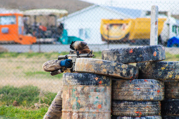 Hiding paintball player takes aim and painted tires take cover.