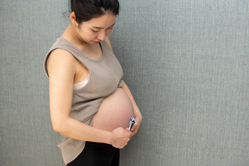A young pregnant Asian woman using a shaver in front of the wall