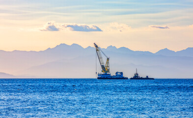 Fototapeta premium sea ship with a crane on the background of a mountain range in the haze