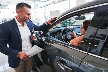 Experienced car showroom manager looking at his female customer