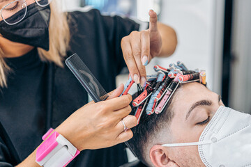 Close up view of a hairdresser curling the hair of a man using a mask