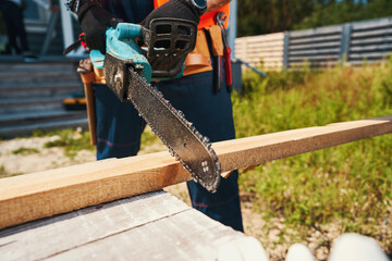 Person sawing off piece of board with chainsaw - obrazy, fototapety, plakaty