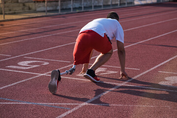 Caucasian male athlete with a prosthetic leg standing at the start on the track at the stadium. Back view. Sport concept.