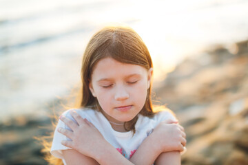 Sad Lonely Caucasian child preteen girl hugs herself with her arms by the sea, toning, negative emotions, emptiness and sadness, calmness and self-focus