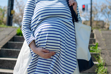 A young pregnant Asian woman going down the stairs with totebag for picnic