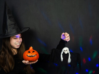 Halloween. Cheerful girl in a witch costume and with a pumpkin celebrating Halloween. Copy space. Black background.
