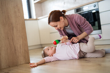 Happy mother with small daughter playing indoors in kitchen, laughing.