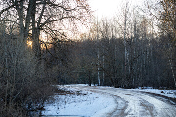 winding country road in Latvian forest in end of winter or early spring, slippery and dangerous ice and snow covered way out of woods