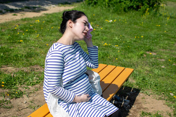 A young pregnant Asian woman sitting on the outside bench and wiping sweat way