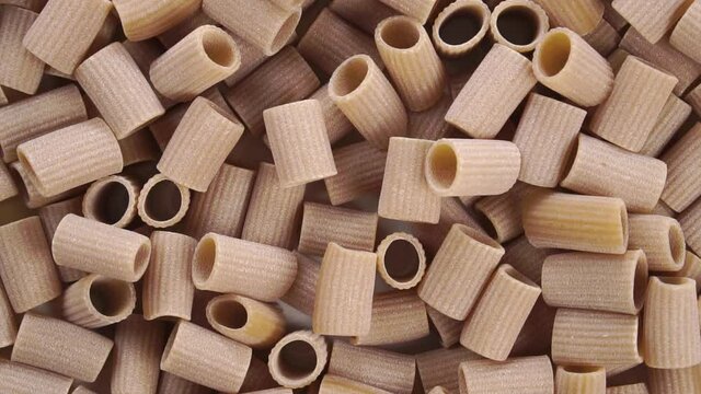A pile of uncooked integral rigatoni pasta. Falling macaroni in slow motion. Top view. Close up