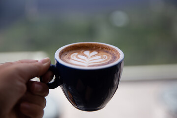 cup of cappuccino with latte art holding by woman with mountain view background