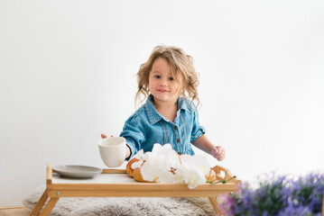 Cute little girl in a denim blue dress. Holds a croissant. Breakfast. Light room. European race.