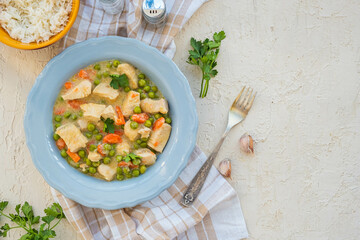 Chicken stew or indian curry with carrots and green peas in a gray plate on a light concrete background. Served with rice.
