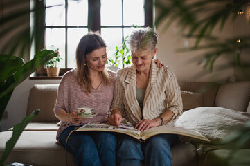 Front view of senior mother with adult daughter indoors at home, looking at family photographs.