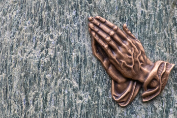 Praying hands as bronze figure on a graveyard grave as religious symbol for faith christianity...