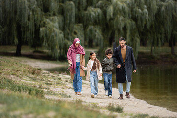 Fototapeta premium Smiling muslim kids walking near parents and lake in park