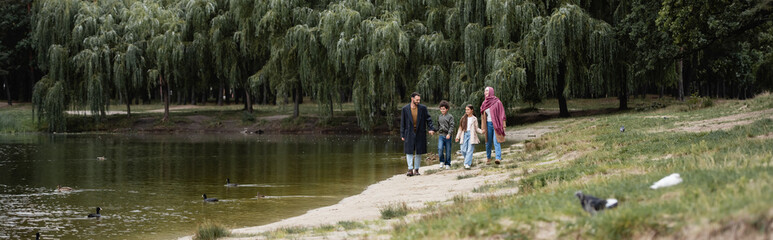 Fototapeta na wymiar Muslim family walking near lake in park, banner