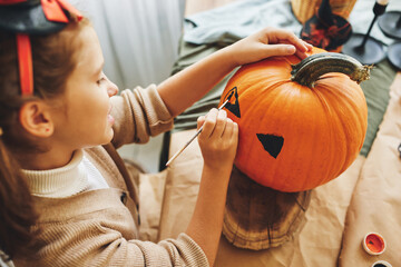 Little kid girl making Jack-o-lantern while preparing for Halloween party at home