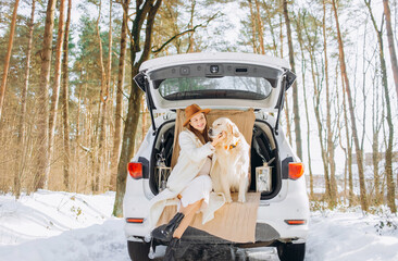 Young woman and cute golden retriever dog sitting in the trunk of a car winter season, traveling.