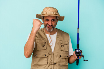 Middle age caucasian fisherman holding rod isolated on blue background  showing fist to camera, aggressive facial expression.