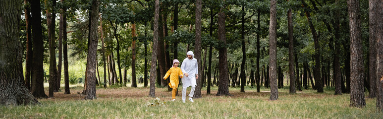 Fototapeta premium Smiling muslim father and son running in park, banner