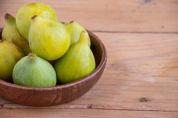 Close-up of green figs in wooden bowl on rustic wooden table, horizontal, with copy space