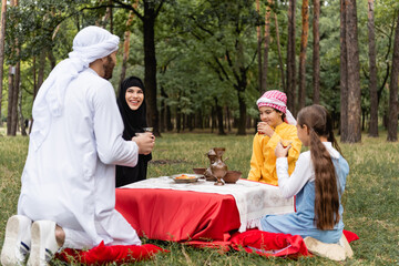 Arabian family holding tea in traditional glasses during picnic in park