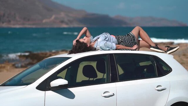 Happy girl lying on a car at seaside. Best friends spend summer time together. The girls are happy and enjoy life. The road by car to the sea. Friendship and love forever. The beauty of Greece.