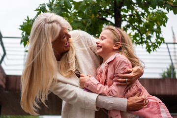 Fototapeta premium A good-looking, modern grandma and granddaughter hug and enjoy together while spending time outdoors on a cloudy, windy day.