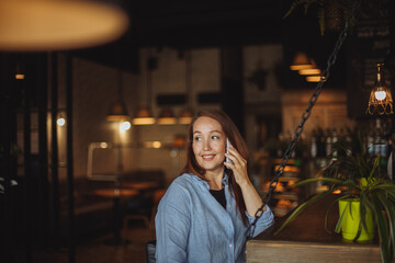 Obraz premium middle-aged woman in a blue shirt uses a mobile phone in a cafe