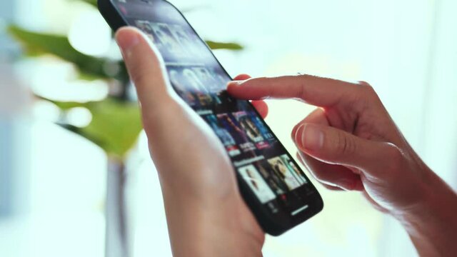 Finger of woman touching scroll page app on mobile phone. Browsing movie video in the internet library to watch film online.
