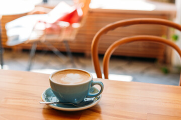 Cup of cappuccino with latte art. Coffee in blue cup on wooden table in cafe. Concept of easy...
